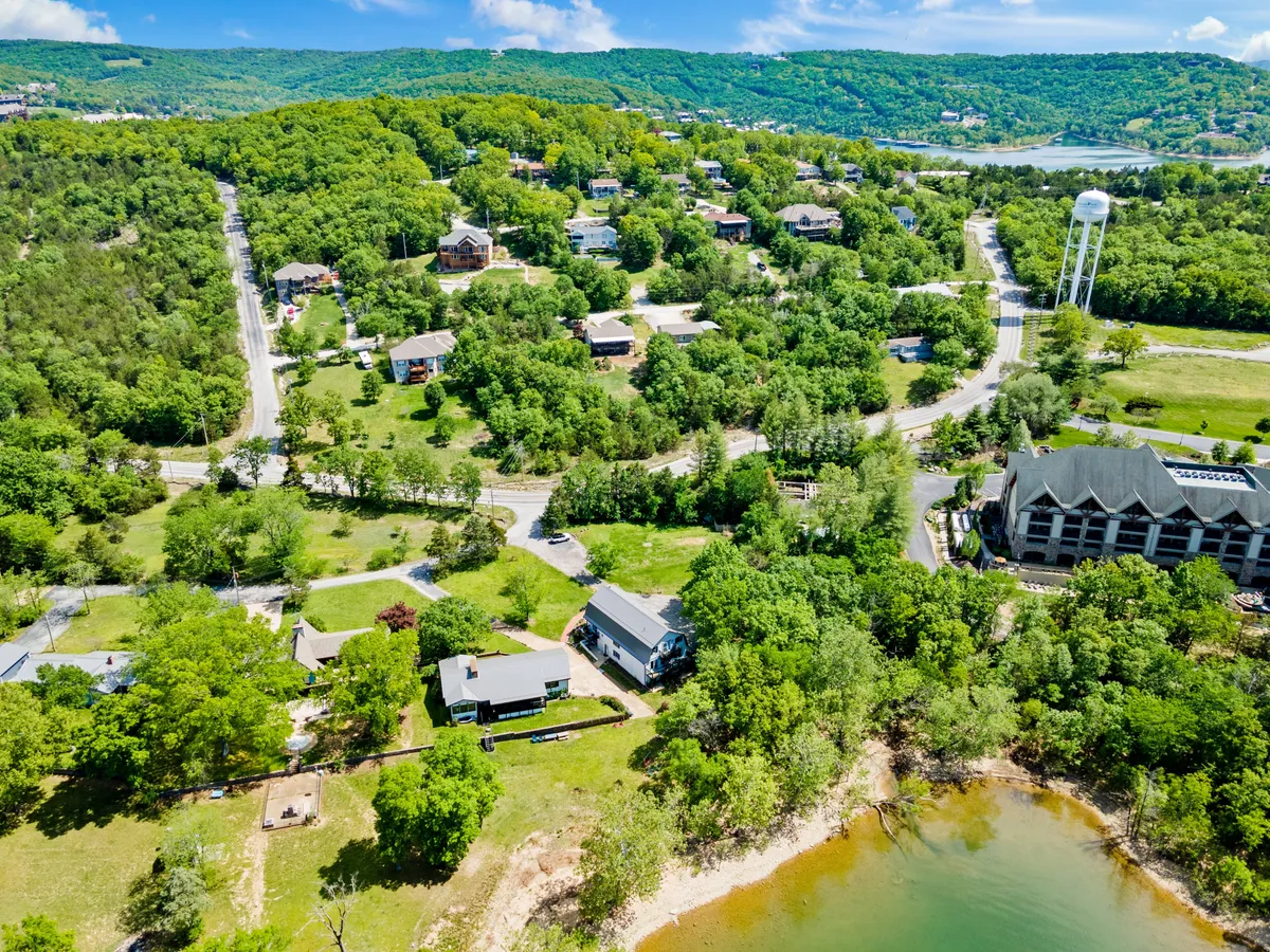 A wide-angle view showing lush green trees, the lake shoreline, and homes nestled within the natural landscape. The image captures the broader environment, hinting at nearby nature trails and opportunities for exploration with pets, as well as the peaceful, natural setting that defines the retreat experience.