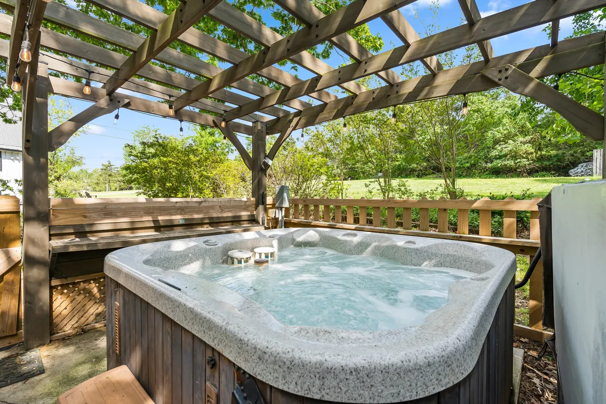 This image features a lakeside hot tub nestled under a wooden pergola surrounded by lush greenery. The inviting setup is situated near the water, with ample space for relaxation and socializing. The proximity to nature and other amenities suggests an ideal spot for unwinding after a day of activities.