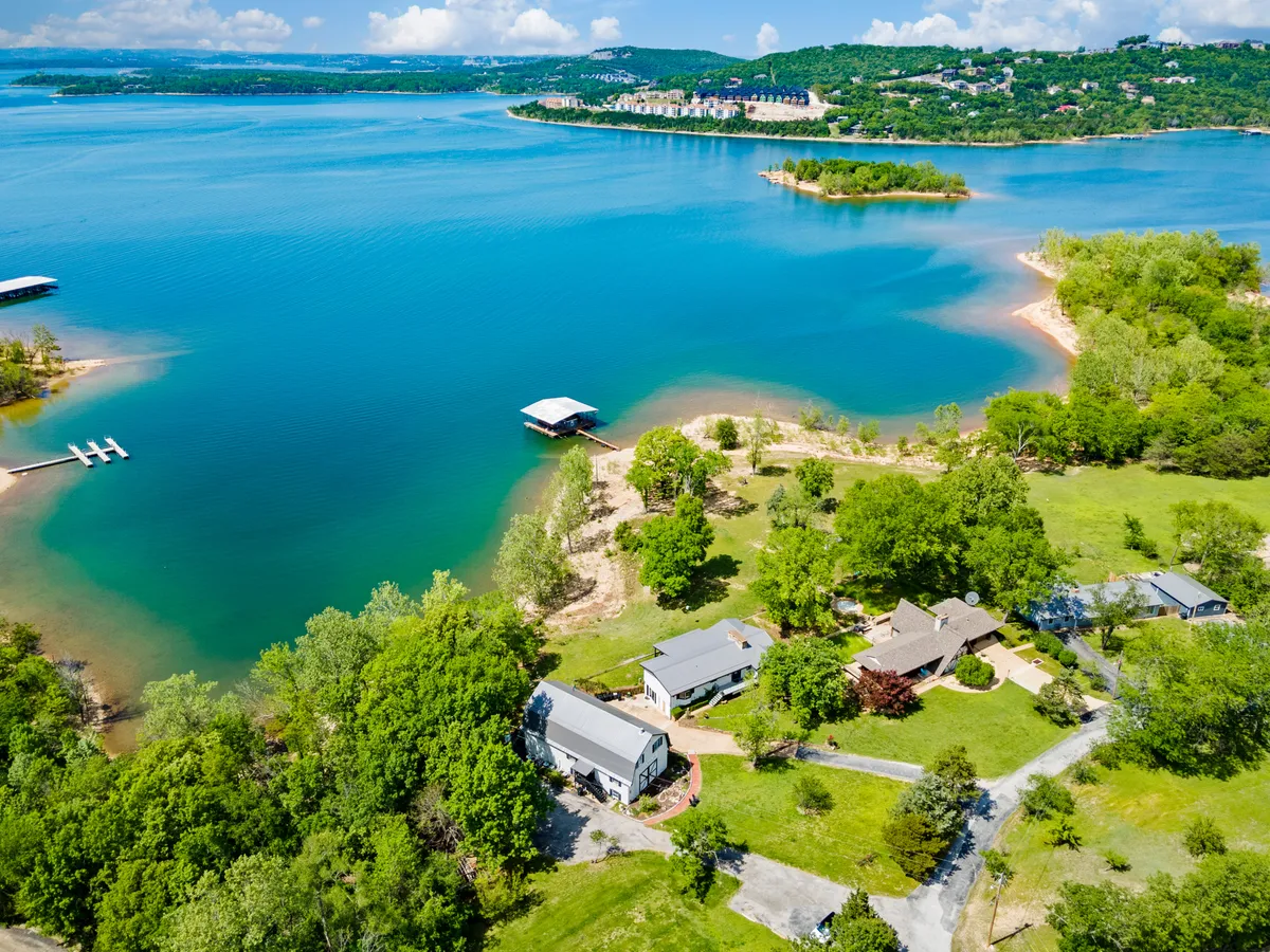 A tranquil lakeside view featuring calm water, boats, nearby houses, and lush trees. The scene shows people boating, fishing, and picnicking along the lake’s edge, with natural trails visible in the background—offering a snapshot of the variety of outdoor activities available right at the water's edge.