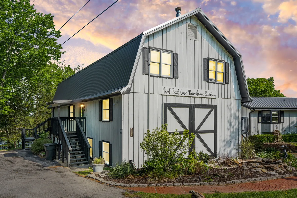 A view of barn-style architecture with a landscaped garden and illuminated windows, setting the scene for family gatherings, outdoor barbecues, and nature walks. The porch offers a vantage point for sunset watchers, while the garden and yard encourage outdoor play and exploration.