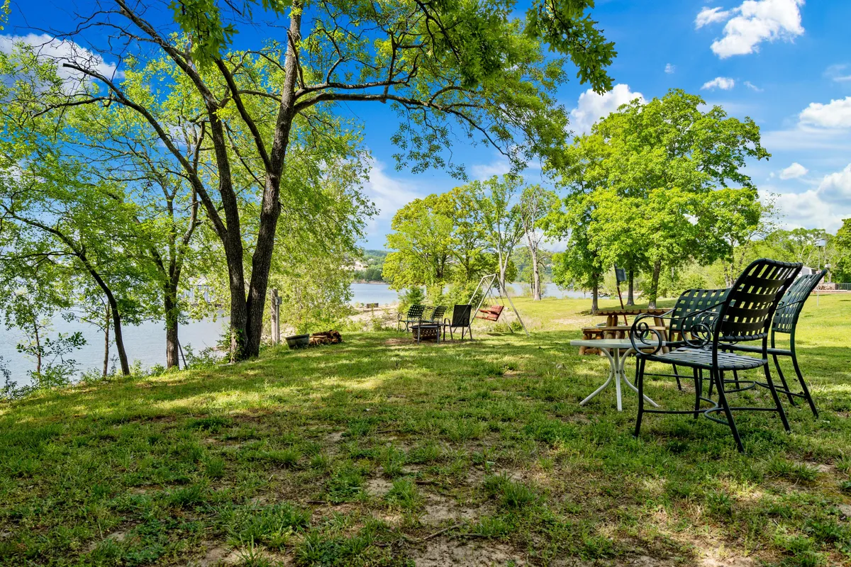 A scenic exterior shot featuring lush greenery, a tranquil river, outdoor seating areas, and a swing set. The environment is perfect for outdoor activities like relaxing, picnicking, fishing, and reading, all set amidst natural beauty.