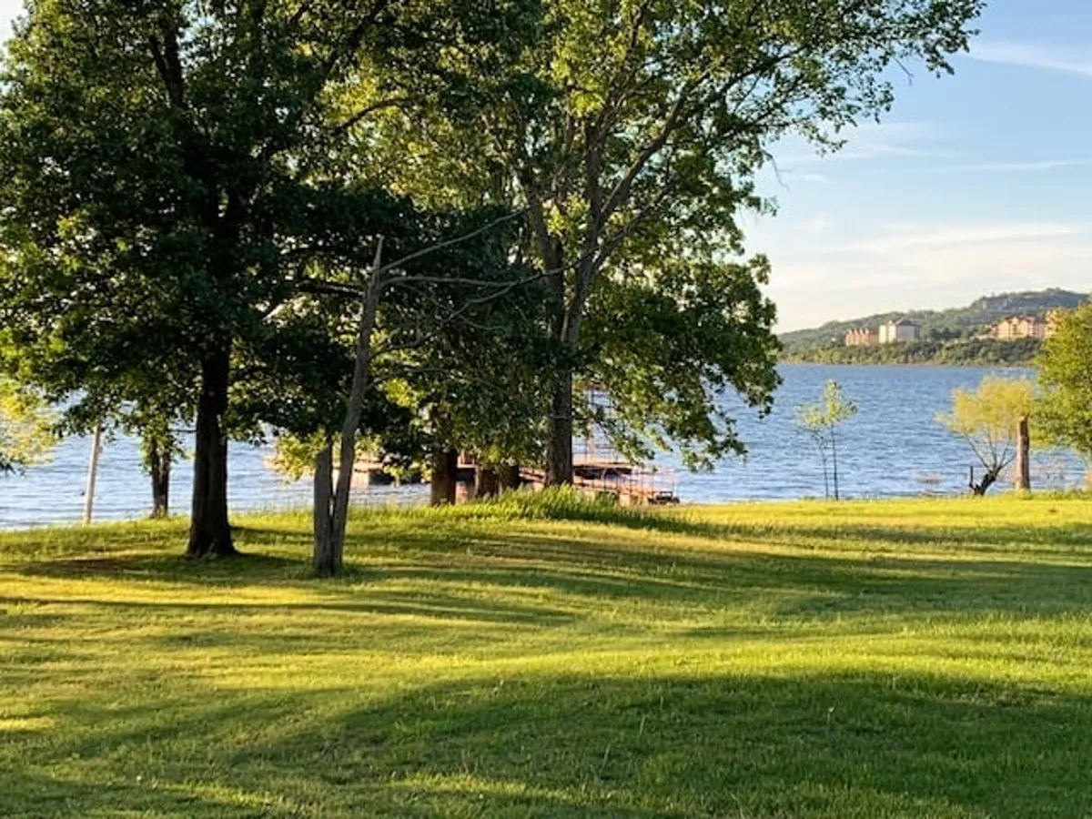 This exterior shot features a tranquil lake bordered by trees, with a pier extending into the water. The image captures the serene environment where guests and their pets can enjoy lakeside walks, picnicking, fishing, or simply soaking in nature. The composition emphasizes direct access to the lake and the abundance of outdoor activities available right outside the property.